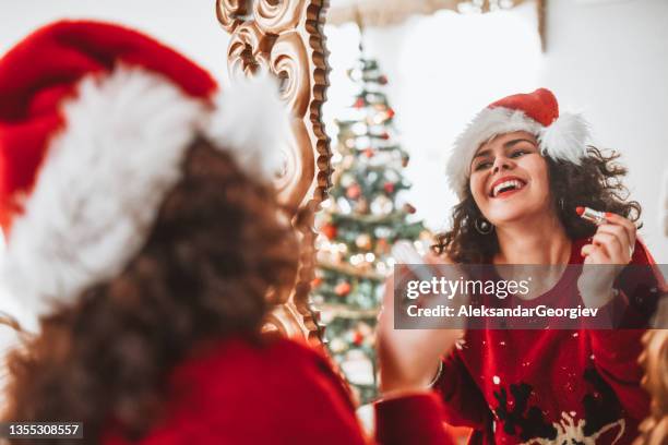 beautiful female with christmas hat putting on lipstick and getting ready for christmas celebration - lipstick mirror stock pictures, royalty-free photos & images