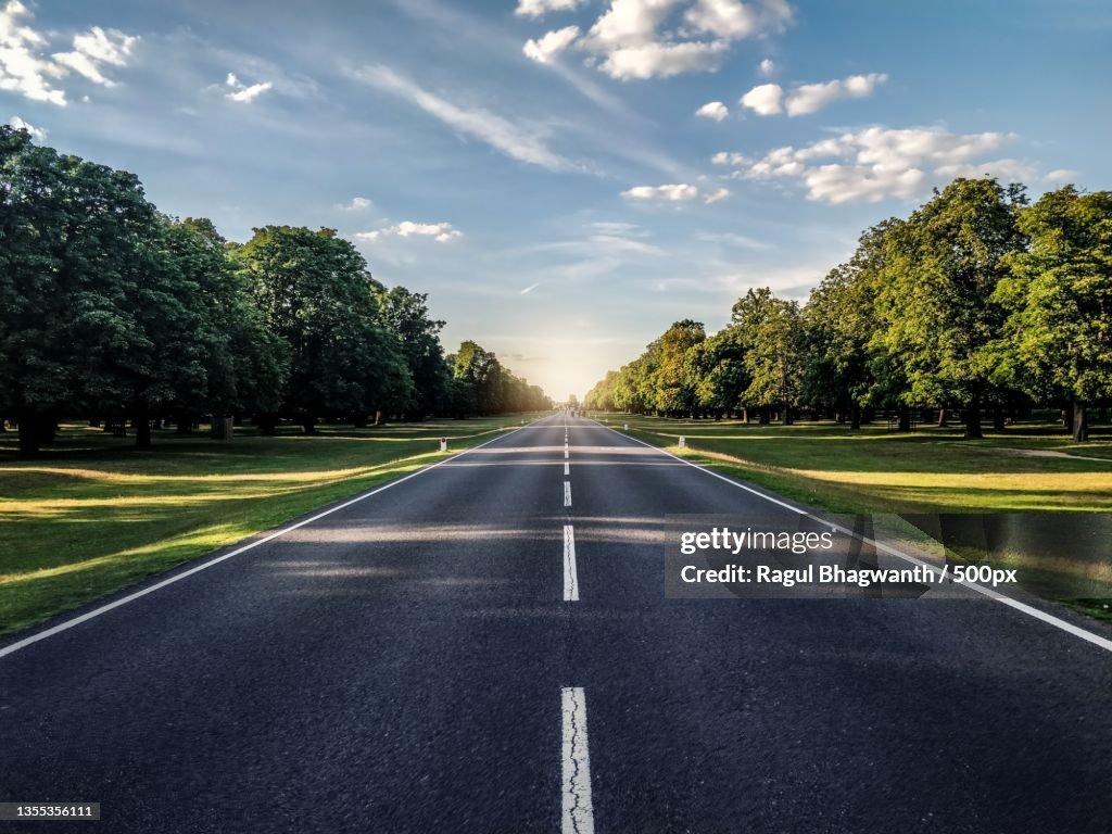 Empty road amidst trees against sky