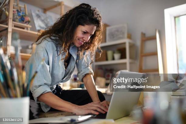 mid adult potter woman, using laptop indoors in art studio small business concept. - small business stock pictures, royalty-free photos & images