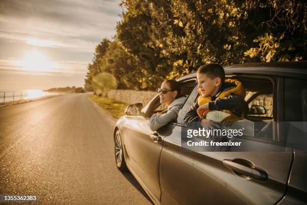 mother and son sitting in car on road and enjoying the sea view during sunset - family car stock pictures, royalty-free photos & images
