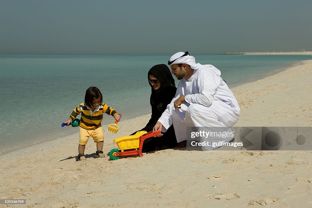 Arab couple playing their son at the beach