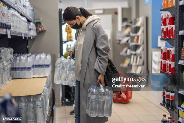 woman with face mask picking plastic water bottles from shelf - mineral water stock pictures, royalty-free photos & images