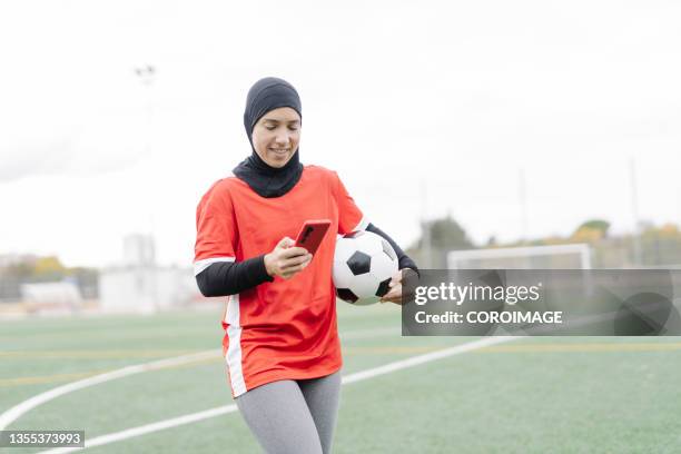 arab female athlete using her mobile phone during a break from training in the field. - football player icon stock pictures, royalty-free photos & images