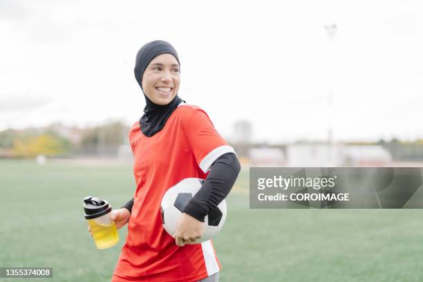 smiling sporty arabic woman drinking something to refresh herself after soccer training on the field. - hoofddoek stockfoto's en -beelden
