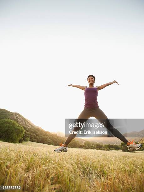 mixed race woman jumping in remote field - breitbeinig stock-fotos und bilder