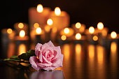 PINK ROSE ON THE GRAVE AND LIGHTED CANDLES UNFOCUSED IN THE BACKGROUND.