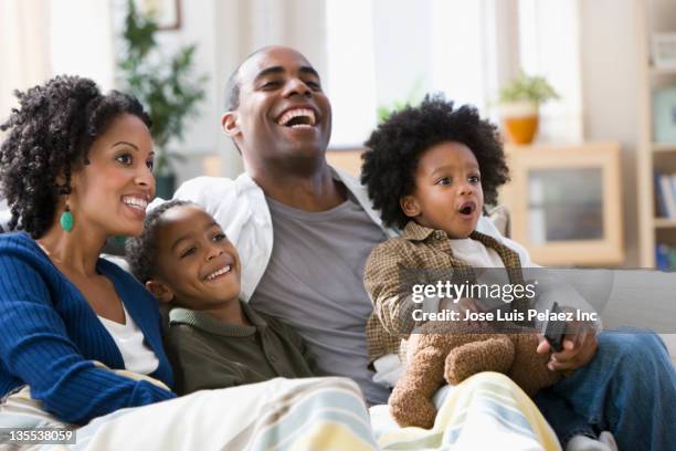 african american family watching television together - family of four in front of house stock-fotos und bilder