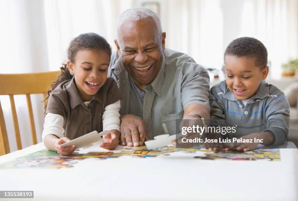 grandfather and grandchildren putting a puzzle together - senior puzzle stock pictures, royalty-free photos & images