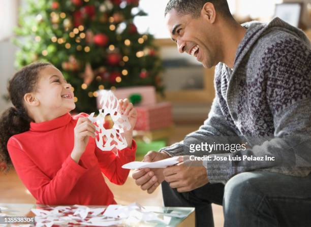 father and daughter making christmas paper snowflakes - paper snowflakes stock-fotos und bilder