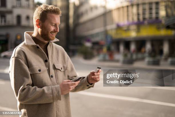 young man using online banking while on a walk on city street. - effortless stock pictures, royalty-free photos & images