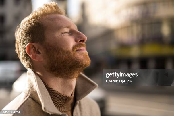 ruhiger junger mann, der auf der straße der stadt meditiert. - man closed eyes stock-fotos und bilder