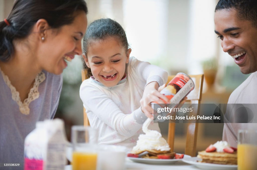 Parents watching daughter putting whipped cream on pancakes