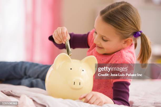 mixed race girl putting money into piggy bank - blonde girl piggy bank stock-fotos und bilder