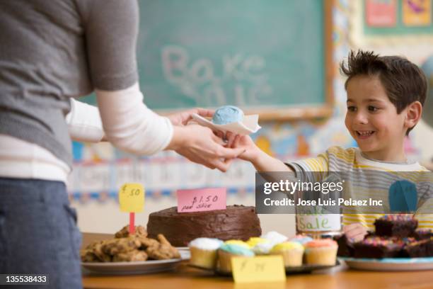 caucasian boy buying cupcake at bake sale - cake sale stock-fotos und bilder