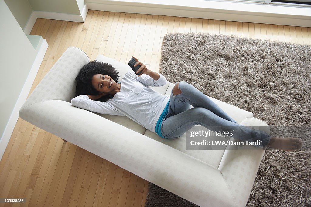 Black woman laying on sofa using cell phone