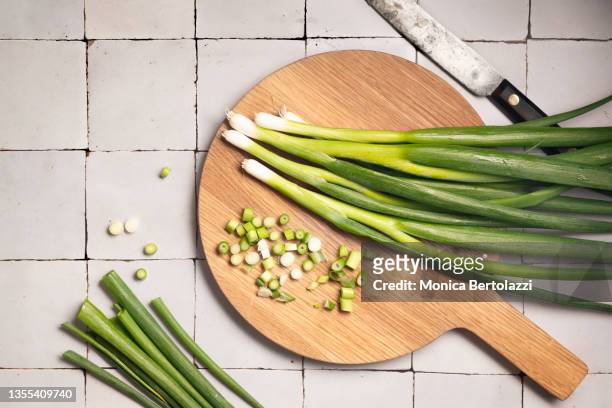 fresh spring onions on wooden board some whole, some cut, with knife - cebolinha capim família das cebolas - fotografias e filmes do acervo
