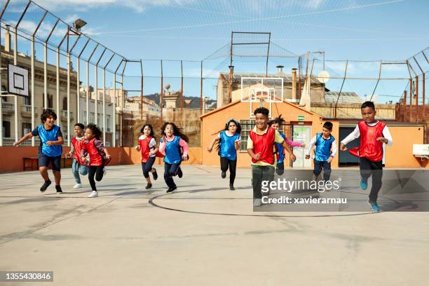 young boys and girls running across schoolyard sports court - naderen stockfoto's en -beelden