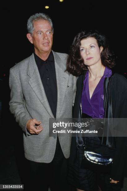 American actor and singer Troy Donahue wearing a grey blazer and a black shirt, and a woman attend an event, circa 1995.