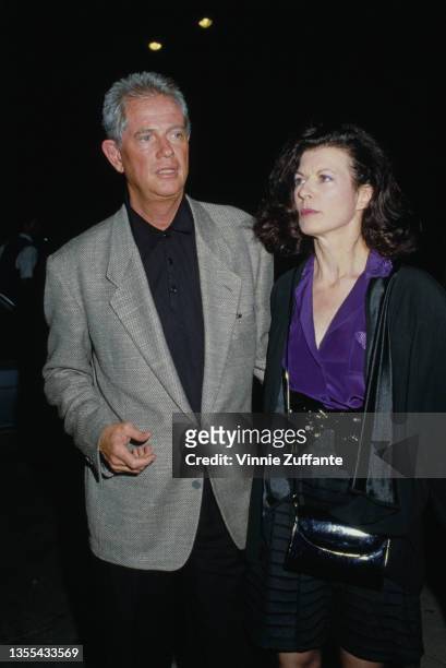American actor and singer Troy Donahue wearing a grey blazer and a black shirt, and a woman attend an event, circa 1995.