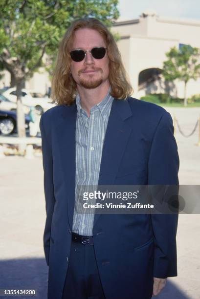 American actor Eric Stoltz, wearing a blue suit with a striped shirt, open at the collar, and sunglasses, 1994.