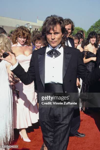 British actor and singer Michael Des Barres, wearing a black tuxedo, black bow tie, and black cummerbund, with his wife, Pamela visible to the left...