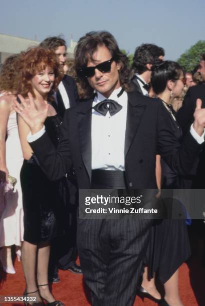British actor and singer Michael Des Barres, wearing a black tuxedo, black bow tie, and black cummerbund, with his wife, Pamela visible to the left...