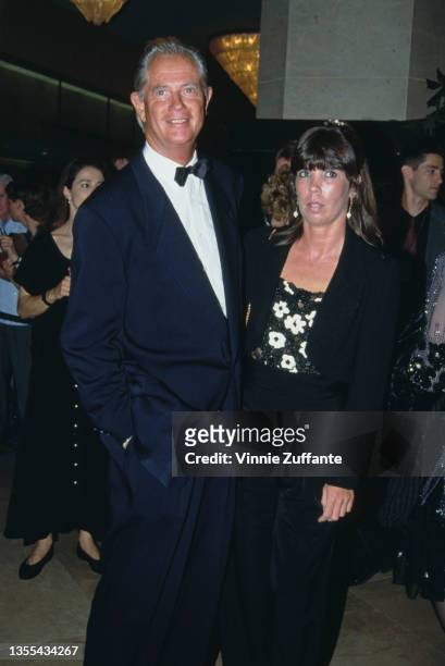 American actor and singer Troy Donahue wearing a dark blue tuxedo and bow tie, and a woman attend an event, circa 1995.