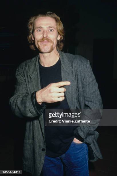 American actor Willem Dafoe, points with one hand while the other is in the pocket of his jeans, attends the Century City premiere of 'Dangerous...
