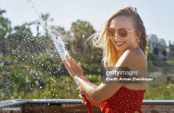 playful woman at the beach using water hose - strapless dress stock-fotos und bilder