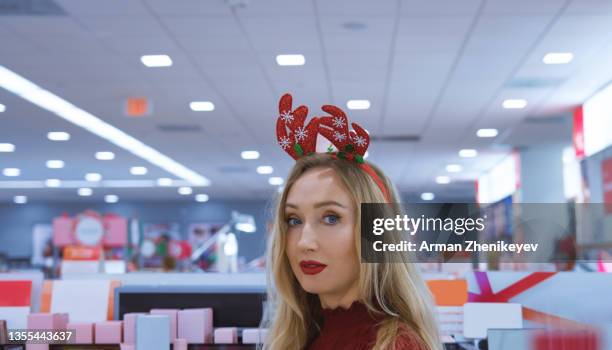 beautiful woman with reindeer headband shopping in a brightly lit store during christmas holidays - geschäftseröffnung stock-fotos und bilder