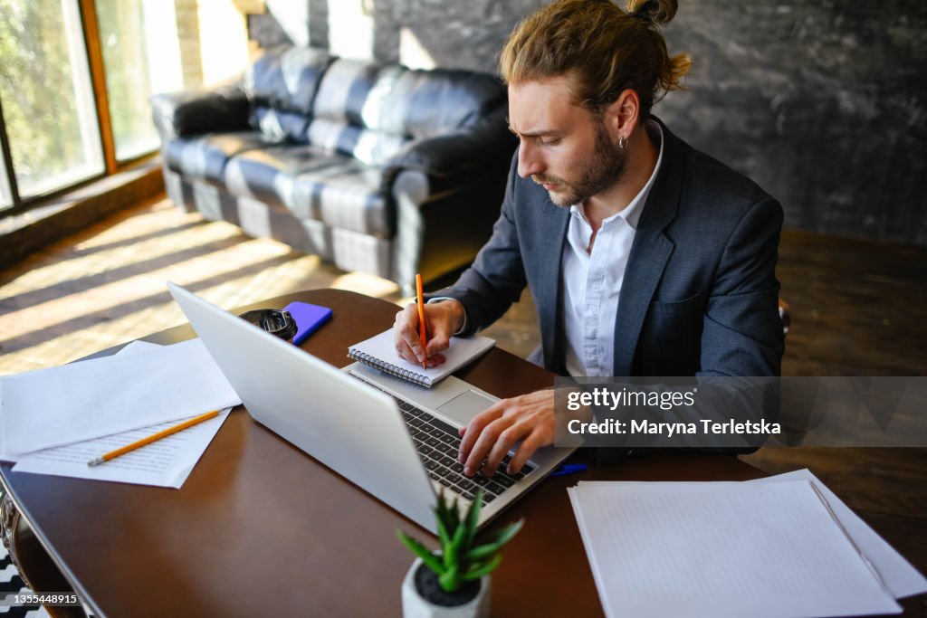 A young guy works at a laptop in a home office.