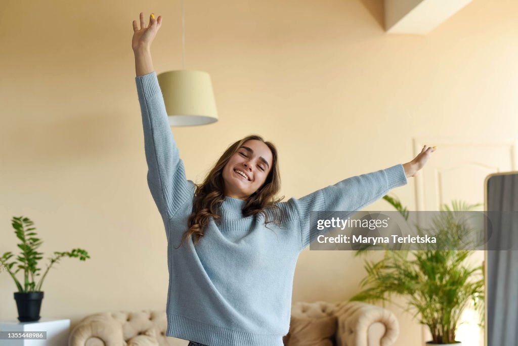 A beautiful girl in a blue sweater is stretching in the room.