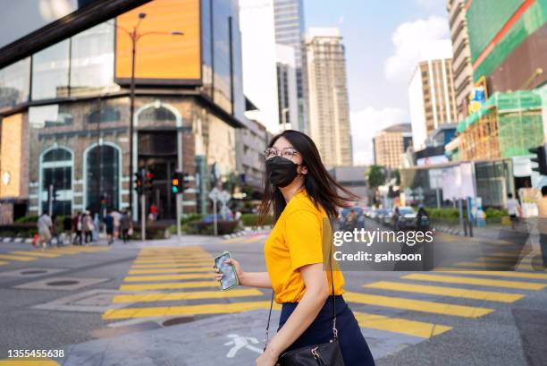 woman in large city, wearing protective facemask - kuala lumpur street stock pictures, royalty-free photos & images