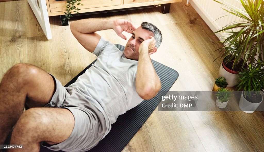 Aufnahme eines reifen Mannes, der Crunches macht, um seinen Kern zu Hause zu stärken