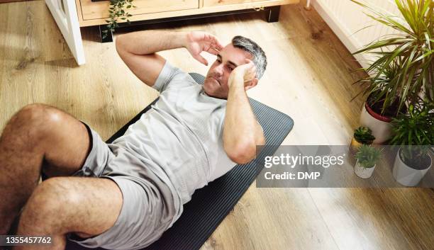 shot of a mature man doing crunches to strengthen his core at home - sit ups stockfoto's en -beelden