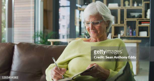 shot of a senior woman writing in a diary at home - diário imagens e fotografias de stock