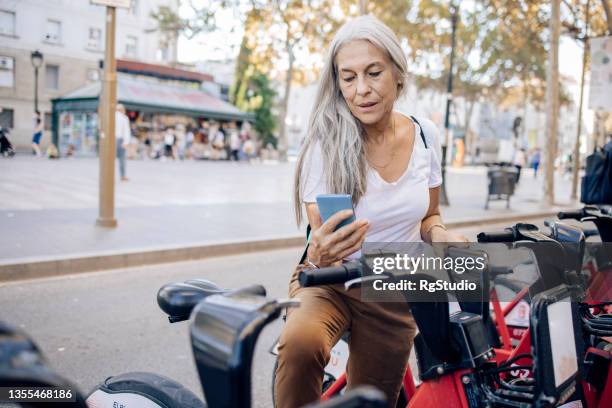 mature female tourist renting an e-bike - bike sharing stock pictures, royalty-free photos & images
