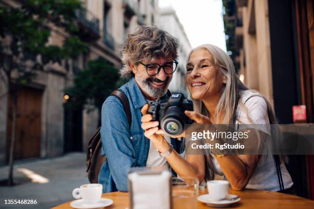 mature couple on vacation enjoying at the cafe and watching their photos - barcelona cafe stock pictures, royalty-free photos & images