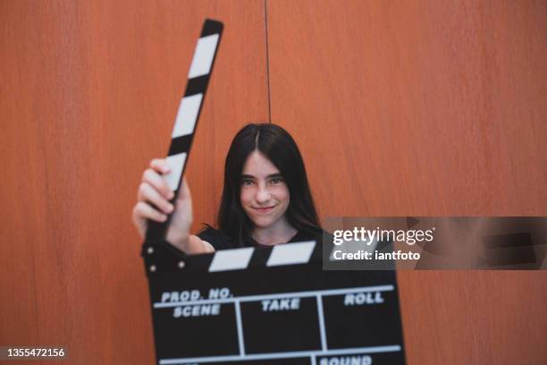 a young girl holding a movie clapboard in front of an orange background. - child film director stock pictures, royalty-free photos & images