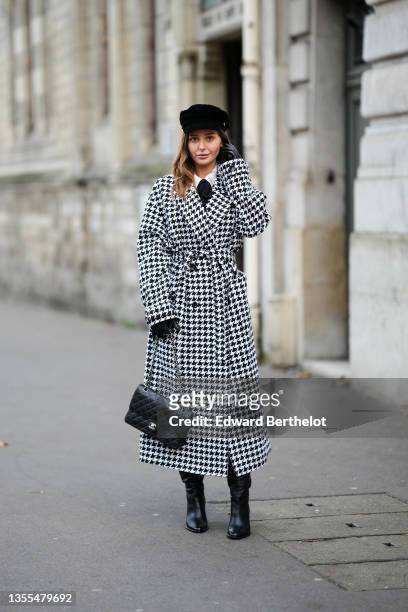 Diane Batoukina wears a black velvet cap, a white shirt, a black wool pullover, a black and white houndstooth print pattern long oversized coat, a...