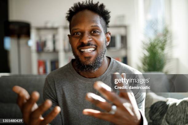 uomo sorridente che ha una videochiamata da casa - review foto e immagini stock