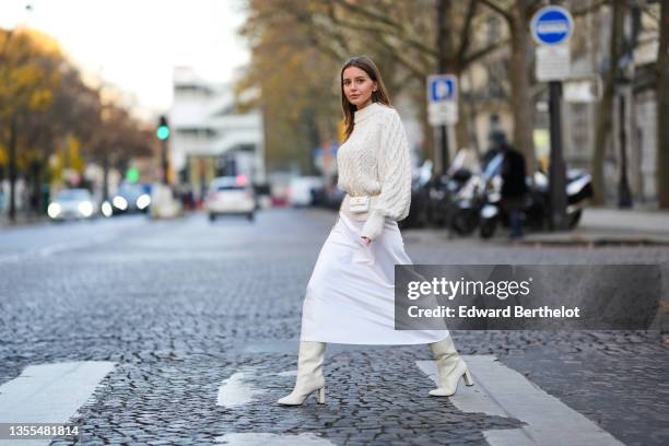 Diane Batoukina wears a white latte braided wool pullover from H&M, a white leather Chanel belt bag, a white silk high waist midi skirt, white latte...