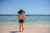7-year boy in blue underwear and a blue hat on the beach looking at the sea