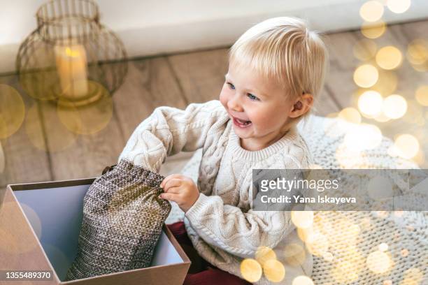 small laughing baby toddler is opening gift box with smile and joy - opening gift stockfoto's en -beelden
