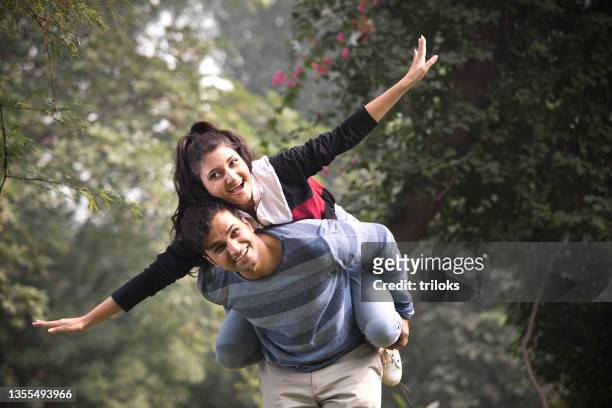 glückliches paar, das eine huckepackfahrt im park genießt - couple india stock-fotos und bilder