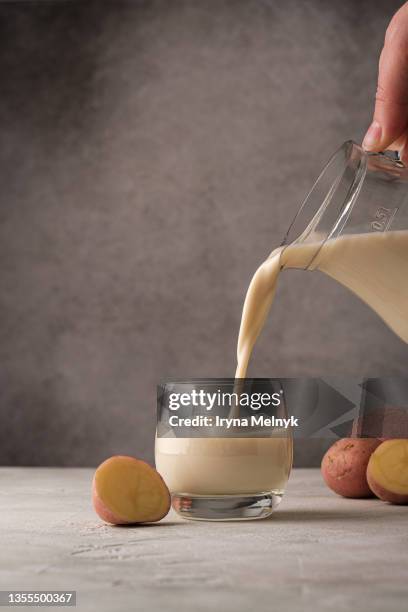 woman is  pouring potato milk alternative non dairy drink in glass from jug on gray background. healthy vegetarian and vegan drink concept - milk jug stock pictures, royalty-free photos & images