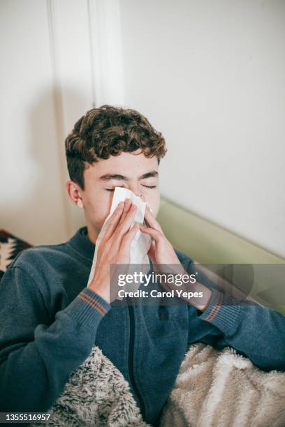 ill boy with flu blowing nose while sitting on sofa at living room - sinusitis stock pictures, royalty-free photos & images