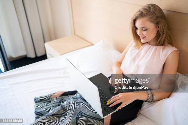 elegante jovem empresária, tendo uma chamada de vídeo no laptop, do quarto de hotel - charming - fotografias e filmes do acervo