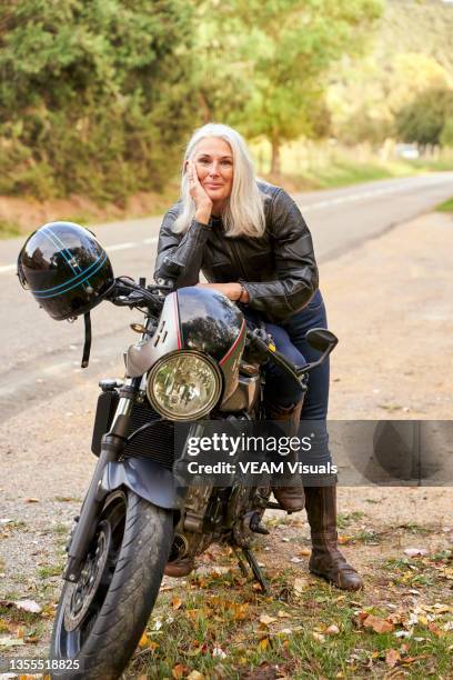 mature woman leaning on her motorbike in the road. - grey hair cool woman stock-fotos und bilder