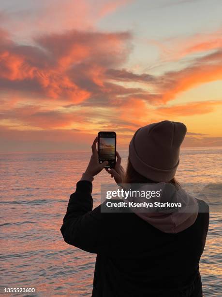 young woman photographing the sunset on the phone back view - prendre photo photos et images de collection